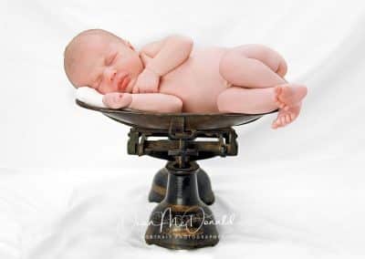 Newborn baby in old fashioned scales on a white sheet.