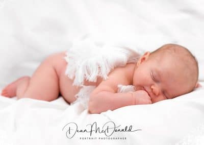 Newborn baby covered by a shawl on a white sheet.