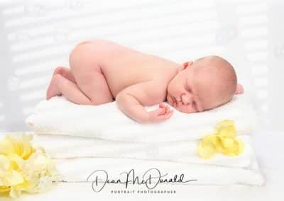 Newborn baby on towels surrounded by yellow flowers and bubbles.