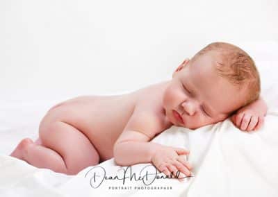 Newborn baby on a white sheet fast asleep.