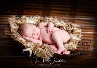 Newborn peacefully curled in fur on a wooden tray.