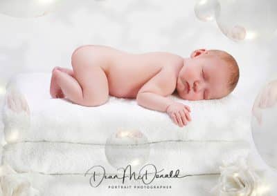 Newborn baby on 3 towels surrounded white roses and reflective bubbles.