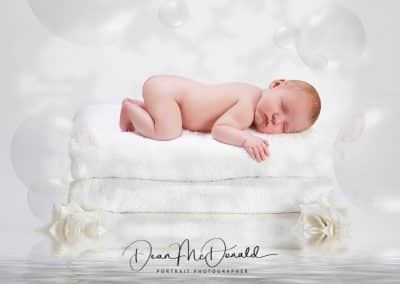 Newborn baby on 3 towels surrounded by water, white roses and bubbles.
