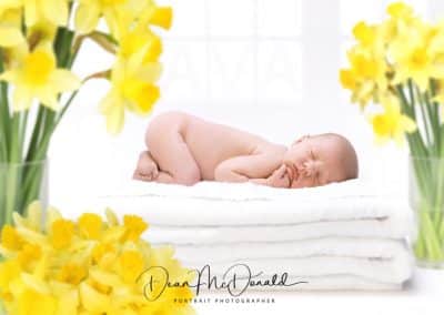 Newborn baby on towels surrounded by daffodils.