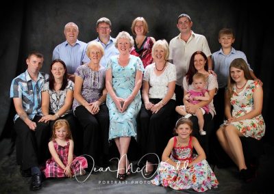 A very large family portrait of 15 people on a traditional studio canvas backdrop.