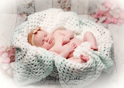 A newborn baby in a round basket covered in thick crochet, wallpaper background.