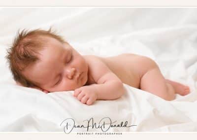 A newborn baby deep asleep on a white sheet.