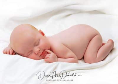 A newborn baby deep in thought on a white sheet.