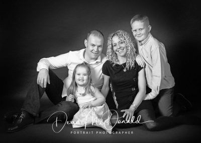 A black and white studio family portrait sitting on the floor.