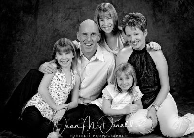 A black and white casual family portrait in matching outfits on a dark canvas background.