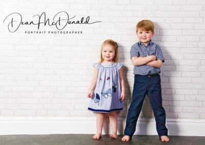 Children's portrait of siblings against a white wall.
