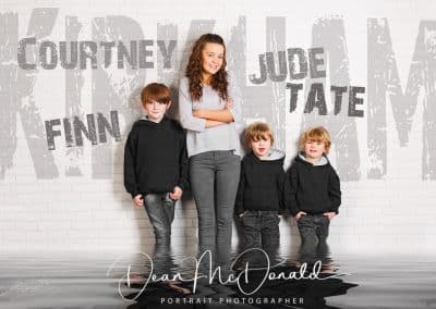 Four children posing against a wall with creative name graffiti knee deep in water.