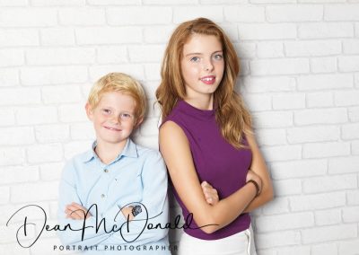 Two childen against a white brick wall.