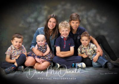 A portrait of of 6 children in coordinated coloured outfits.