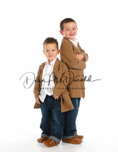 Two boys in blue jeans, white shirts and brown coats, in a casual pose.