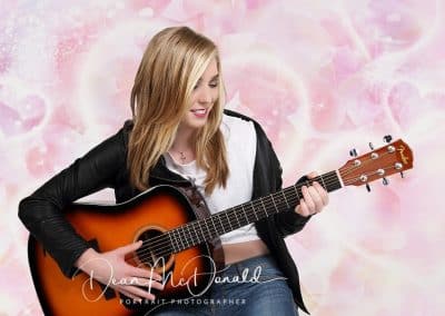 Girl playing guitar against pink background.