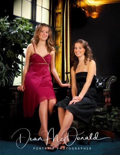 Two women in elegant evening dresses seated at a desk.