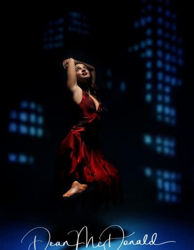 Dancer in a flowing red dress against a blue skyrise backdrop.