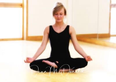 A teenager in a black outfit making a yoga pose.