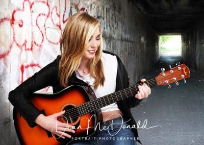 A young blonde girl playing guitar in a tunnel.