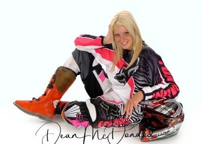 A teenager sitting on floor in a motocross outfit with helmet.