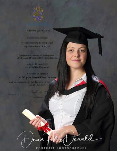 Graduate holding diploma in academic attire. Diploma text as background image.
