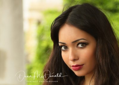 Outdoor portrait of a young woman with a lush greenery background.
