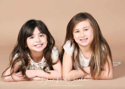 Two girls posing on a neutral background.