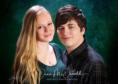 Teenage siblings posing against a green backdrop.