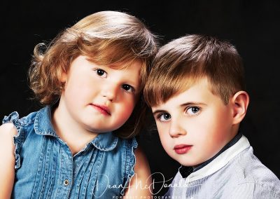 Two young children smiling against dark background.
